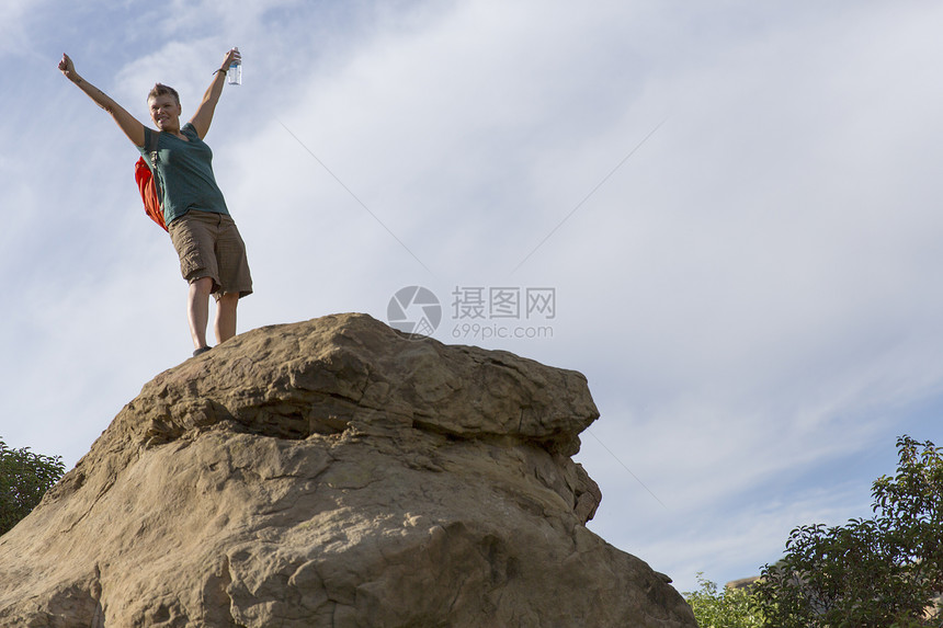 在岩石顶上的女徒步旅行者举起手臂图片