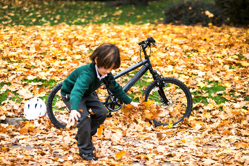 男孩在公园骑自行车玩秋叶图片