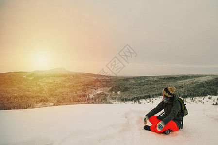雪地上的女人在覆盖着风景坐在山上看日落的景色图片