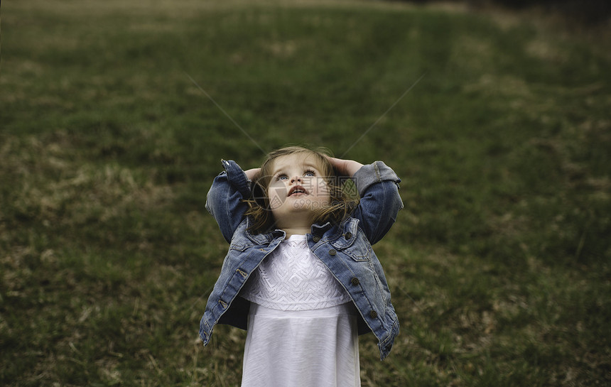 小女孩在草地上双手抬头仰望天空图片