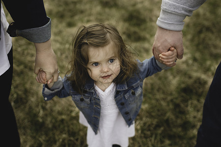 小女孩牵着父母的手在户外行走图片