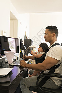 父亲与婴儿在载体中笔记本电脑上工作图片