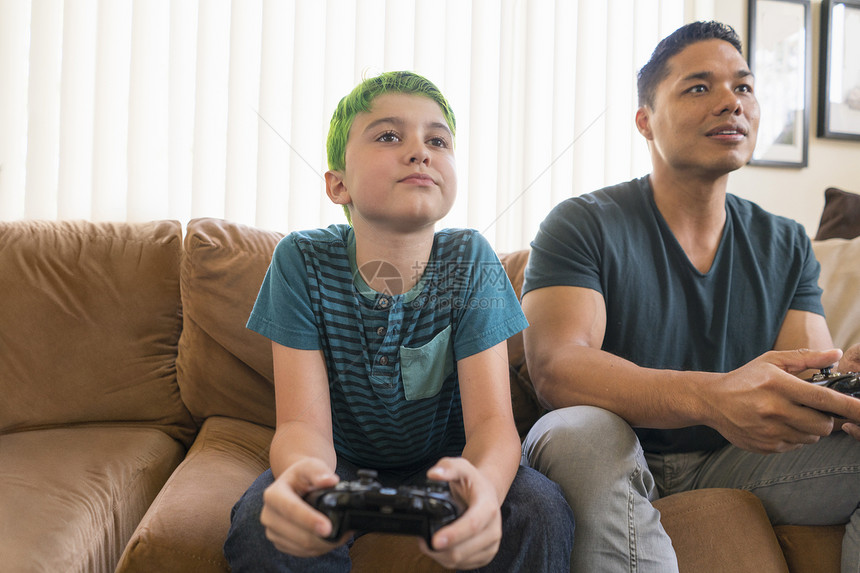 父亲和儿子在沙发上玩电游戏图片
