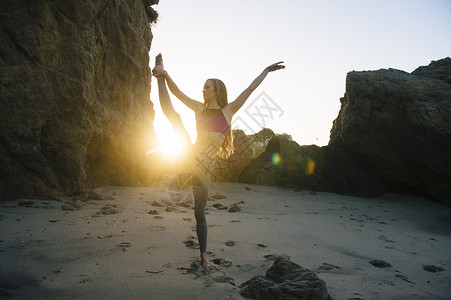 年轻女芭蕾舞者在海滩上拉腿图片