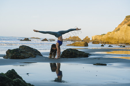 倒立劈叉年轻女舞者在海滩上倒立背景