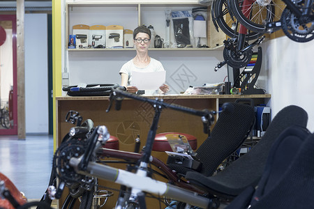 自行车工作坊的妇女在柜台后面看文件图片