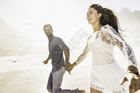 在南非开普敦的日光海滩上手牵奔跑的情侣背景图片