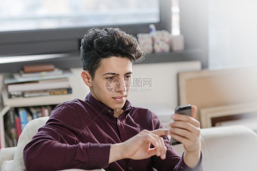 年轻人在沙发上用智能手机发短信图片