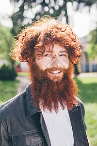 公园里长着红色卷发和胡子的年轻男潮人肖像图片