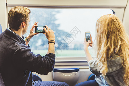 火的照片素材在意大利火车厢窗口拍摄智能手机照片的年轻夫妇背景