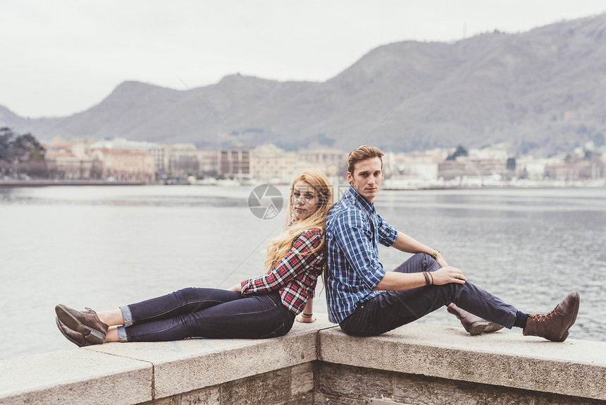 意大利科莫湖港口背靠背坐着的一对年轻夫妇图片
