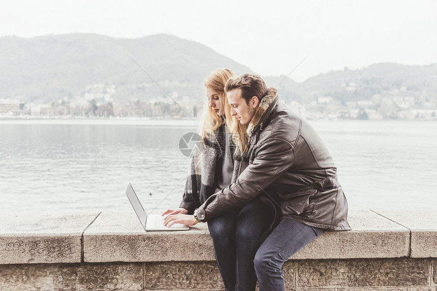 在意大利科莫湖港口墙的同笔记本电脑打字的夫妇图片