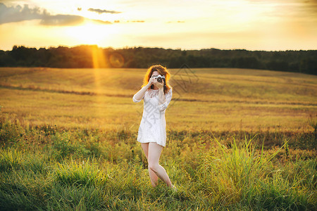 草丛里拿着照相机拍照的年轻女性图片