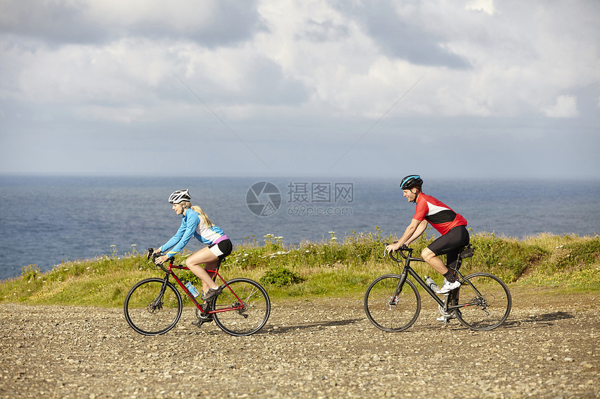 运动员骑自行车在俯视海洋的砂砾路上图片