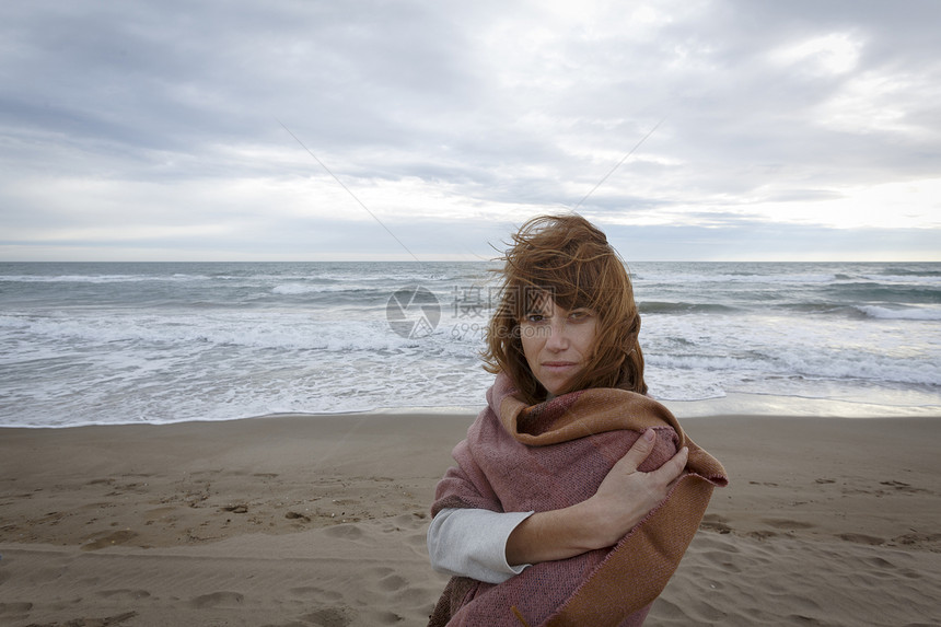 海滩上的女人裹着毯子的海边看着镜头图片