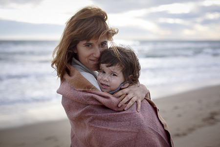 被裹着毛毯的母亲和女儿在沙滩上图片