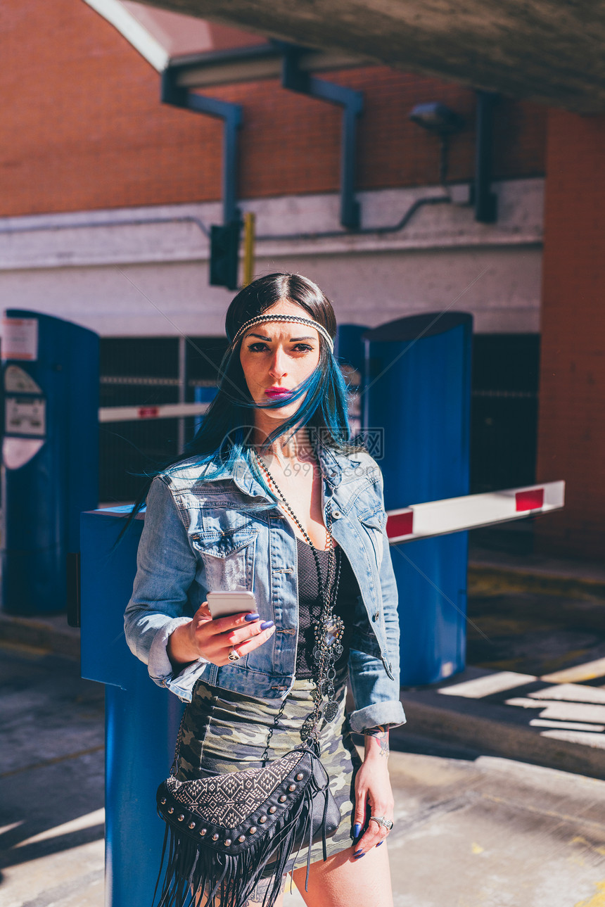 在城市住宅区使用智能手机的染有蓝色头发的年轻女子图片