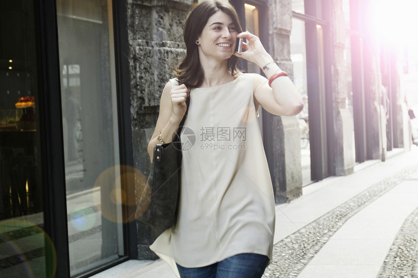 在意大利米兰老街上漫步时使用智能手机的妇女图片