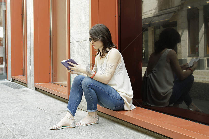 意大利米兰坐在商店前阅读的女性图片