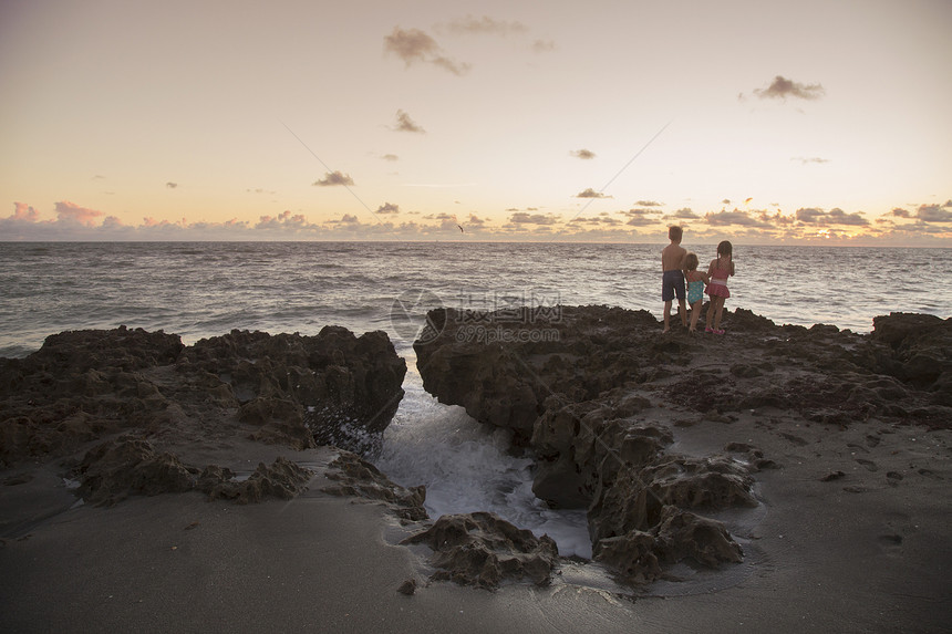 在海边岩石上看日出的小孩们图片