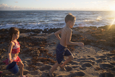男孩和妹妹在海滩上奔跑图片