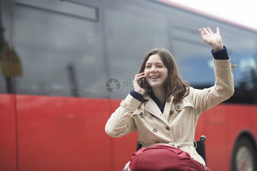 轮椅上从城市公共汽车站挥手的年轻妇女图片