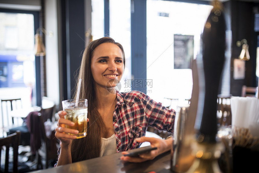 在酒吧拿着手机和酒杯的年轻女子图片