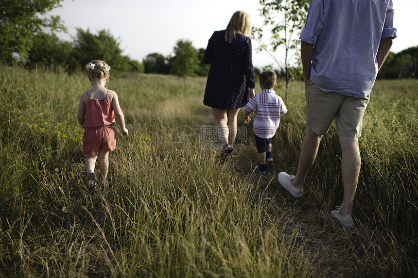 中年父母在草地上带男孩和女孩漫步的后视图图片
