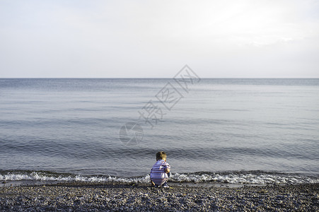 在海滩边蹲下玩耍的小男孩图片