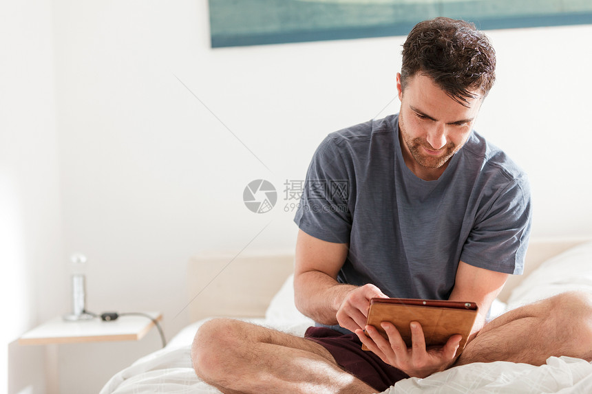 男人用数字平板电脑坐在床上图片