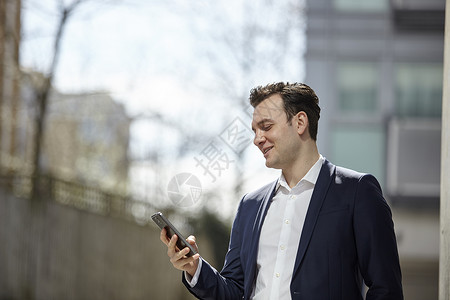 联合王国伦敦办公室外阅读智能手机短信的商人图片