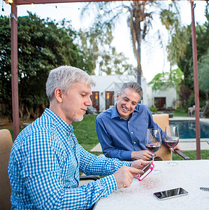两个成熟男子在花园派对桌上观看智能手机触摸屏图片