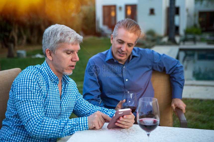 两个成熟男子在花园聚会桌上使用智能手机图片
