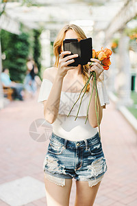 年轻女孩站在户外拿着玫瑰花使用智能手机图片