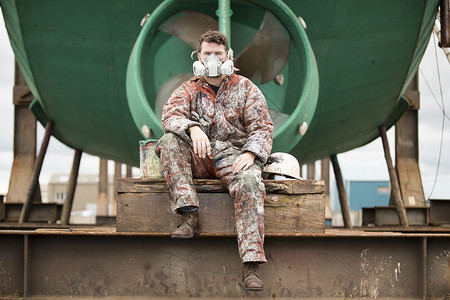 在船上油漆工场绿体前身戴保护面罩的男船舶油漆工肖像背景图片