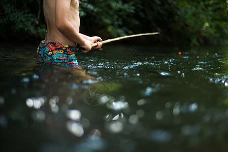 男孩握着鱼竿在溪水中钓鱼图片