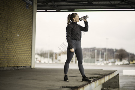 女跑者在仓库平台上饮用瓶装水图片
