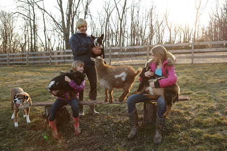 户外母亲和女儿抱山羊和宠物狗图片
