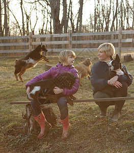 母亲和女儿户外拥抱山羊和宠物狗图片