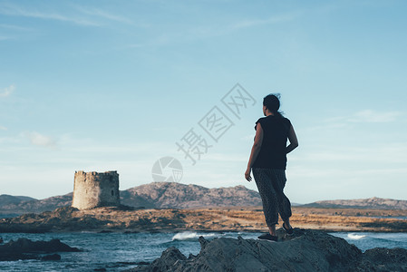 意大利萨萨里斯廷蒂诺一名妇女站在岩石上望着大海对面废弃的灯塔图片