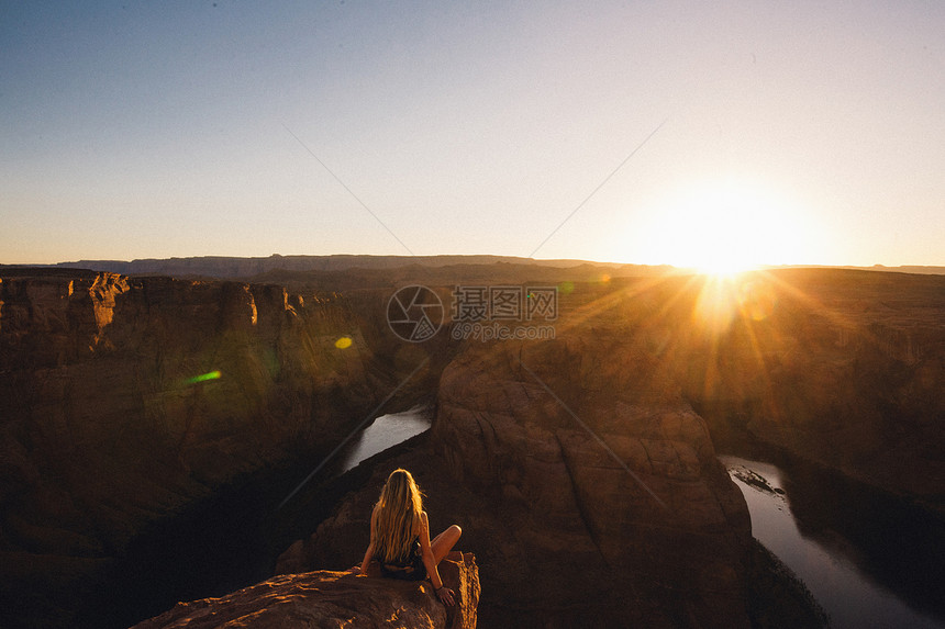 美国亚利桑那州马蹄本德坐在山顶上看日落的女性图片