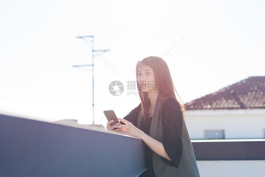 年轻女在使用智能手机的同时从城市屋顶露台看外图片