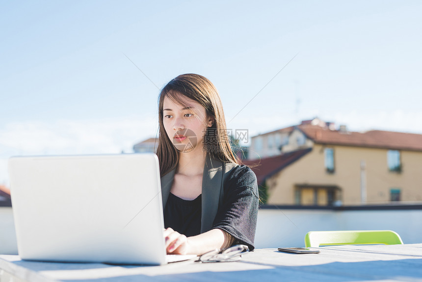 城市屋顶露台的年轻妇女用笔记本电脑打字图片