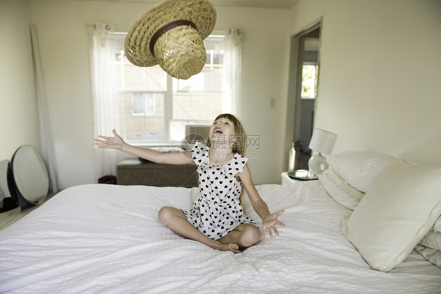 年轻女孩坐在床上把草帽扔在空气中图片