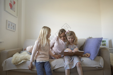 妈妈卧在沙发上为女儿们读故事图片