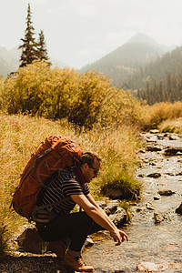 背包坐在小溪旁边的男子图片
