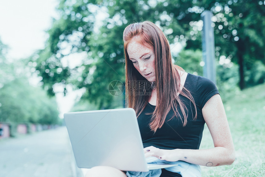 坐在公园里用笔记本电脑打字的年轻妇女图片