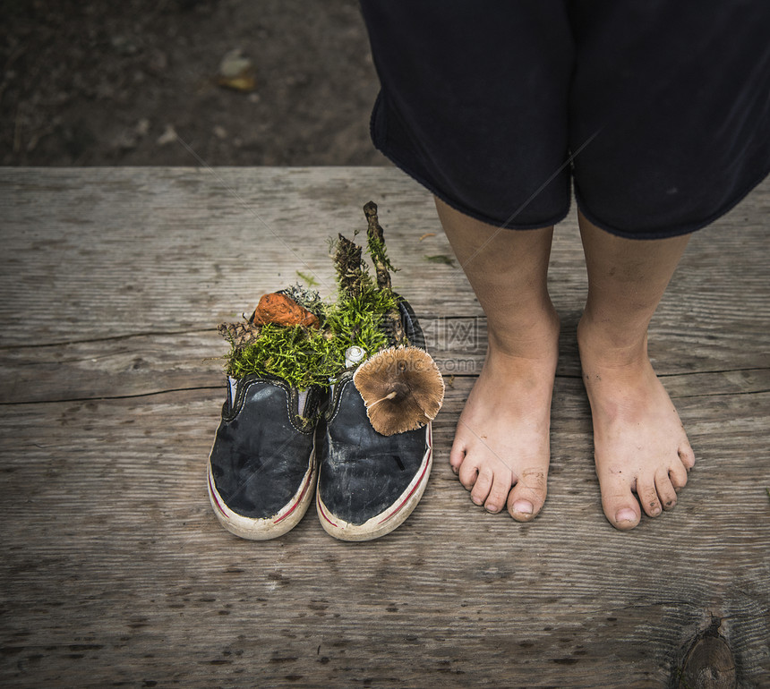 男孩的赤脚站在塞满植物的鞋边图片