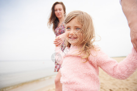女孩笑着牵着父母的手走在沙滩上图片