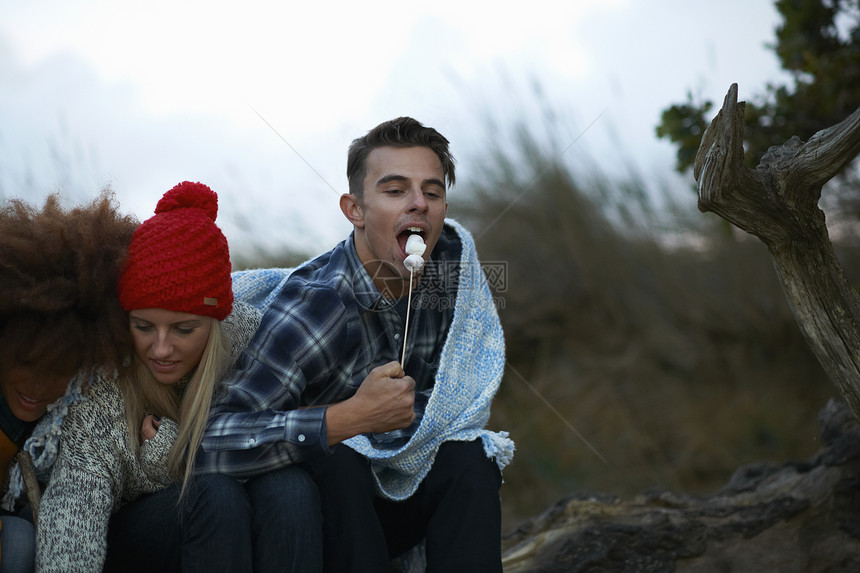 在黄昏海滩吃烤棉花糖的青年朋友图片